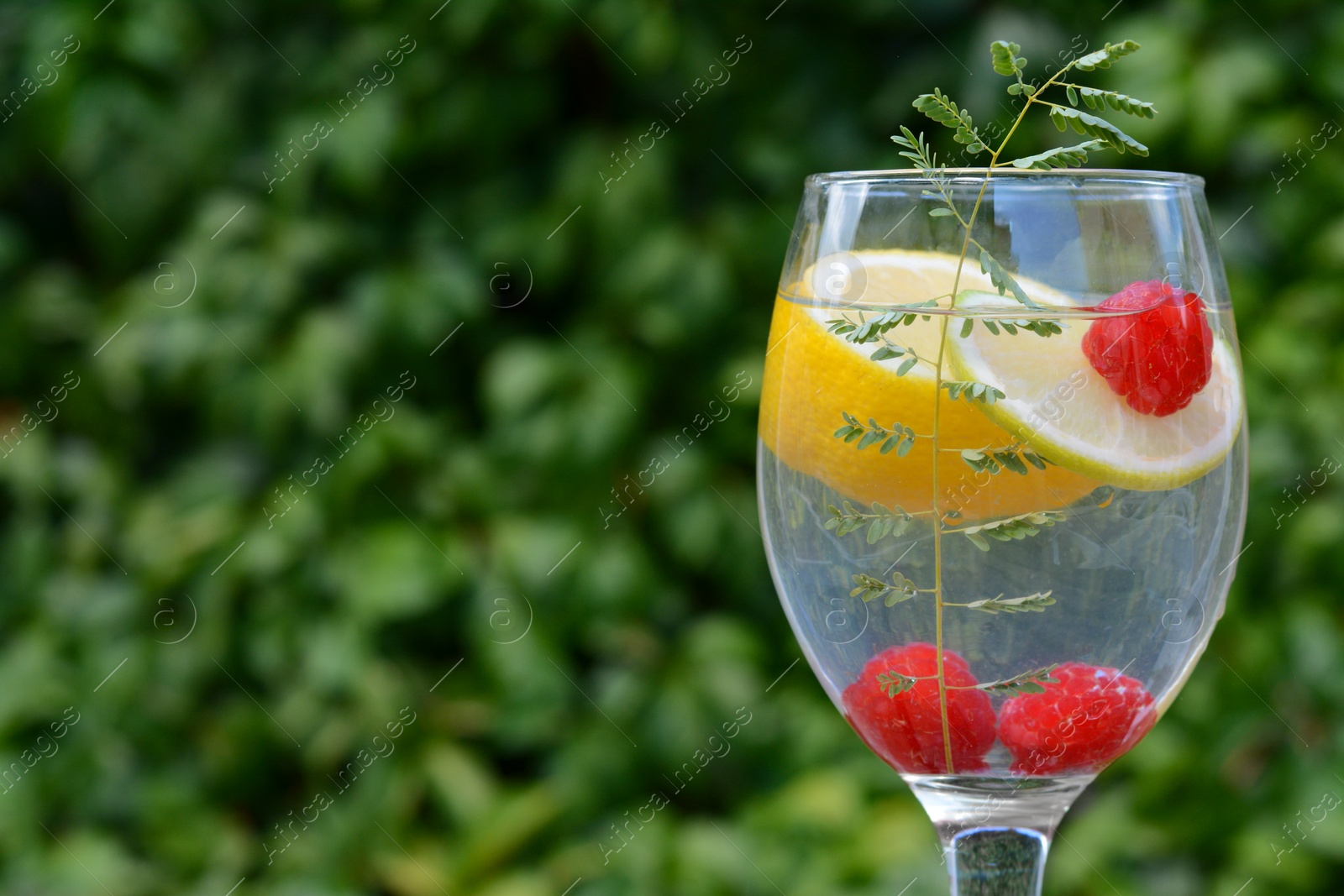 Photo of Delicious refreshing lemonade with raspberries against green blurred background, closeup. Space for text