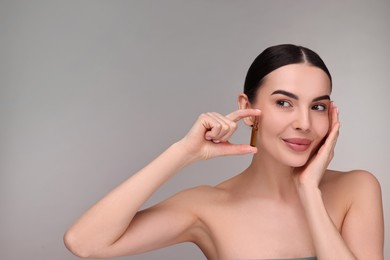 Photo of Beautiful young woman holding skincare ampoule on grey background. Space for text