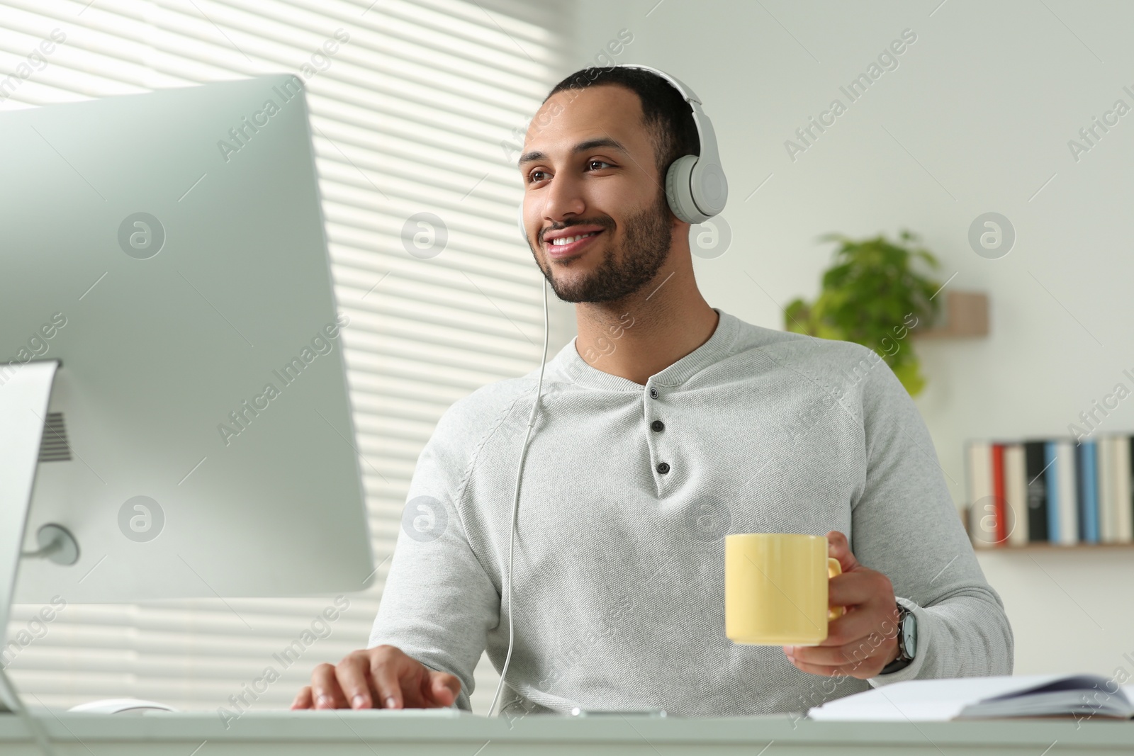 Photo of Young man with headphones working on computer at desk in room. Home office