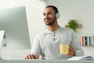 Young man with headphones working on computer at desk in room. Home office