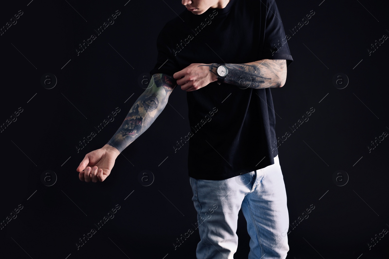 Photo of Young man with tattoos on black background, closeup