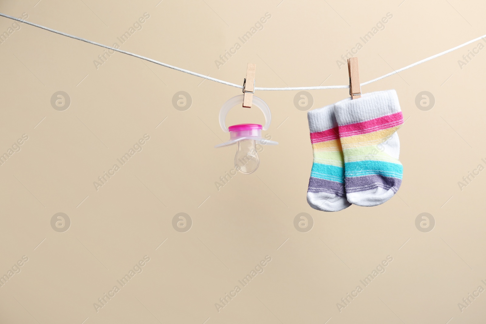 Photo of Small socks and pacifier hanging on washing line against color background, space for text. Baby accessories