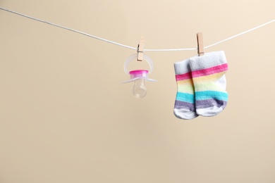 Photo of Small socks and pacifier hanging on washing line against color background, space for text. Baby accessories