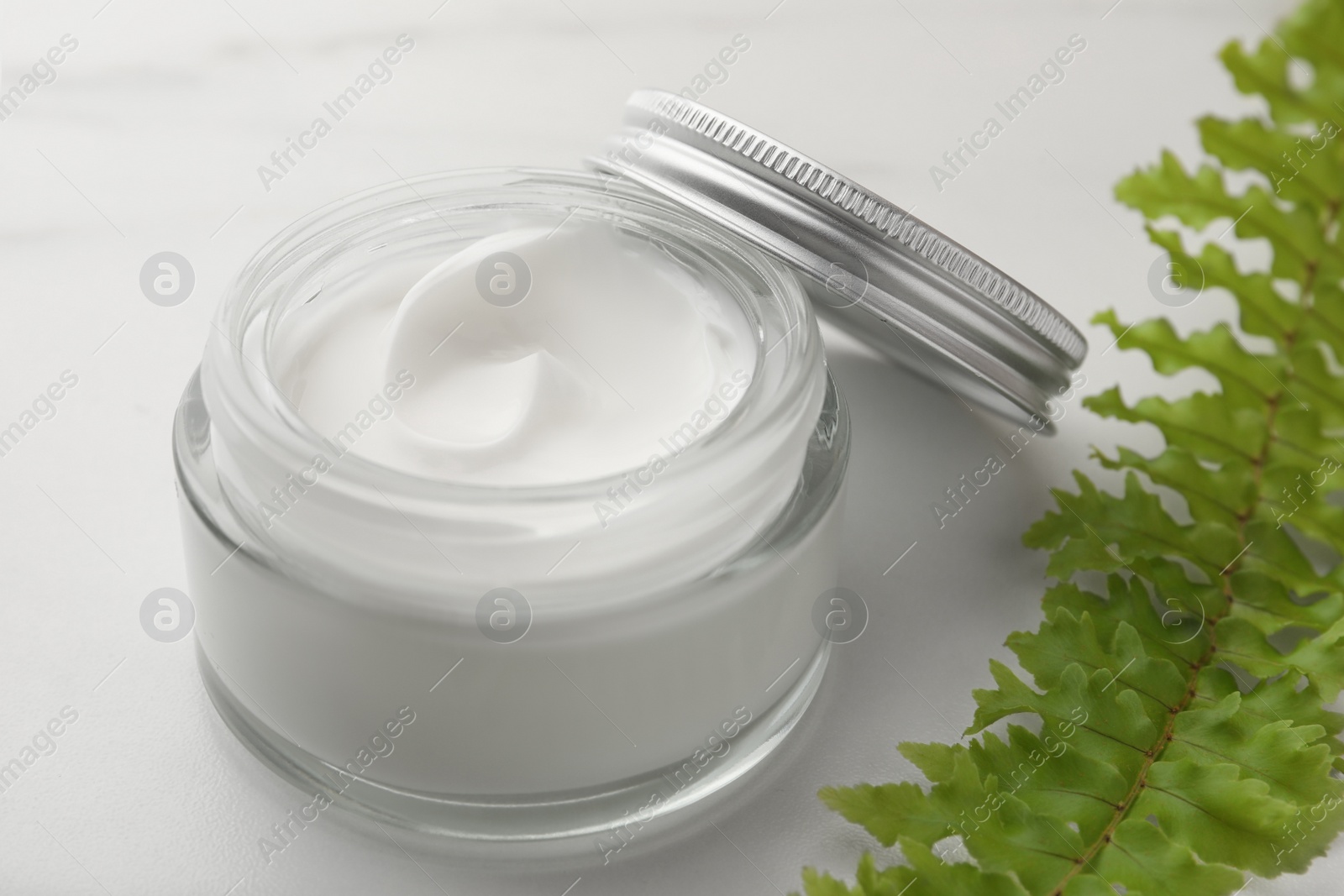 Photo of Glass jar of face cream and green plant on white marble table