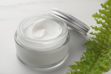 Glass jar of face cream and green plant on white marble table