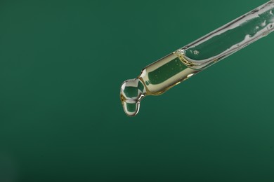 Photo of Dripping hydrophilic oil from pipette on green background, closeup. Space for text