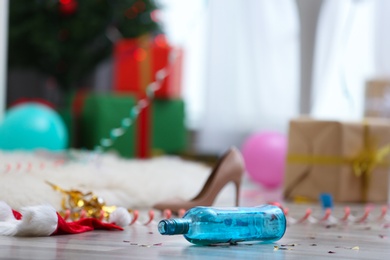 Empty bottle and Santa hat on messy floor. Chaos after party