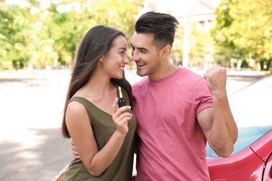 Photo of Happy young couple with key standing near new car on road