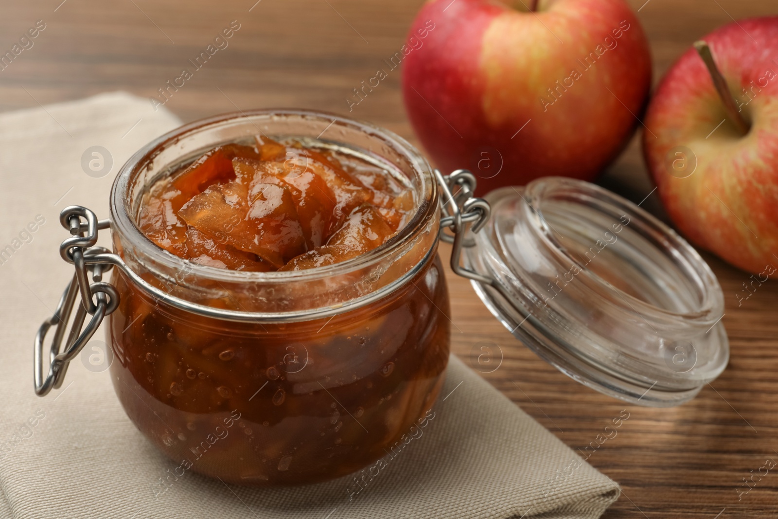 Photo of Tasty apple jam in glass jar and fresh fruits on wooden table, closeup