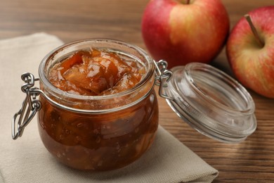 Photo of Tasty apple jam in glass jar and fresh fruits on wooden table, closeup