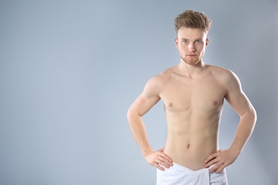 Photo of Portrait of young man with slim body in towel on grey background. Space for text