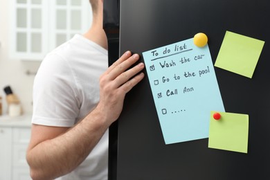 Photo of Man near refrigerator with to do list on door in kitchen, closeup