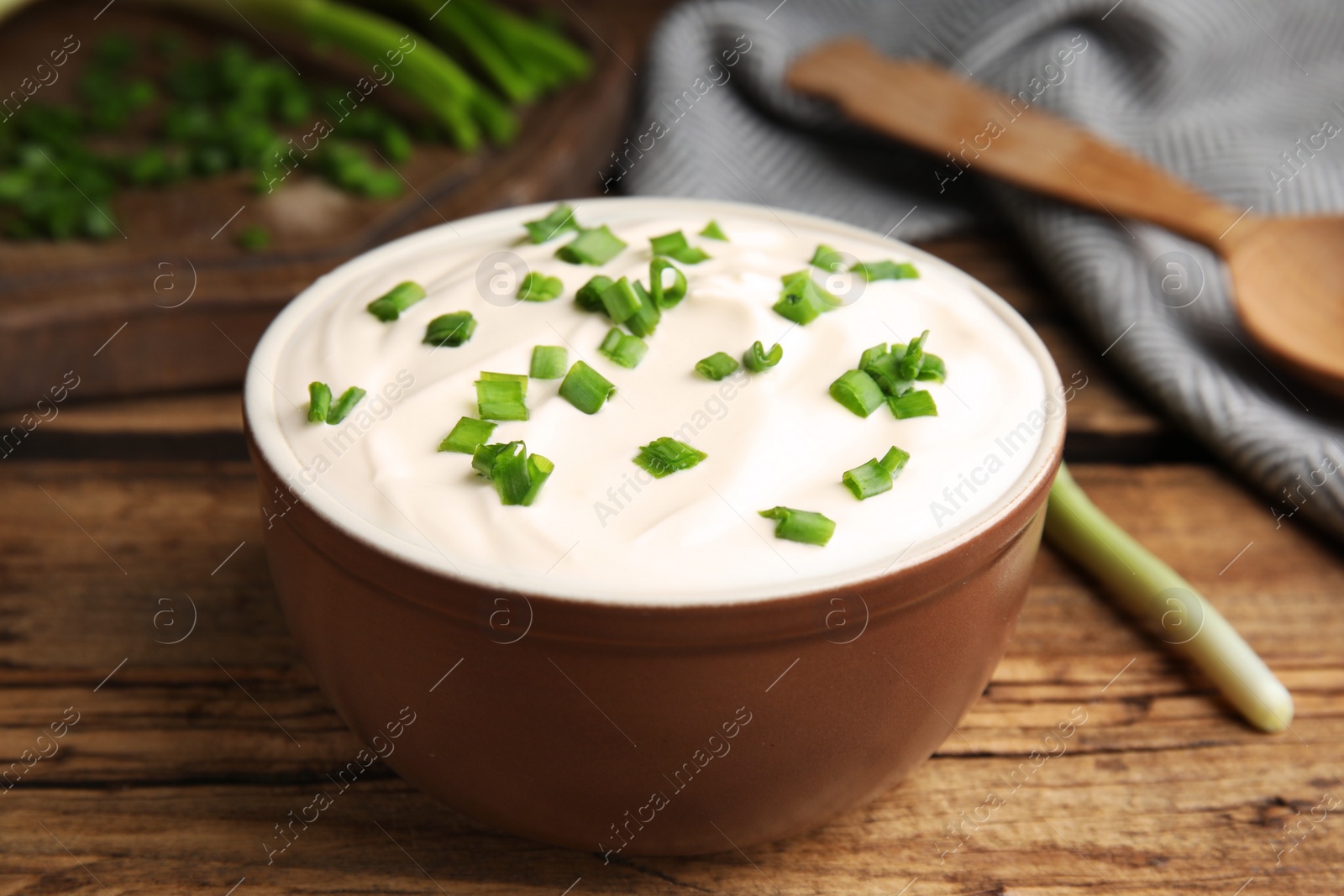 Photo of Fresh sour cream with onion on wooden table, closeup