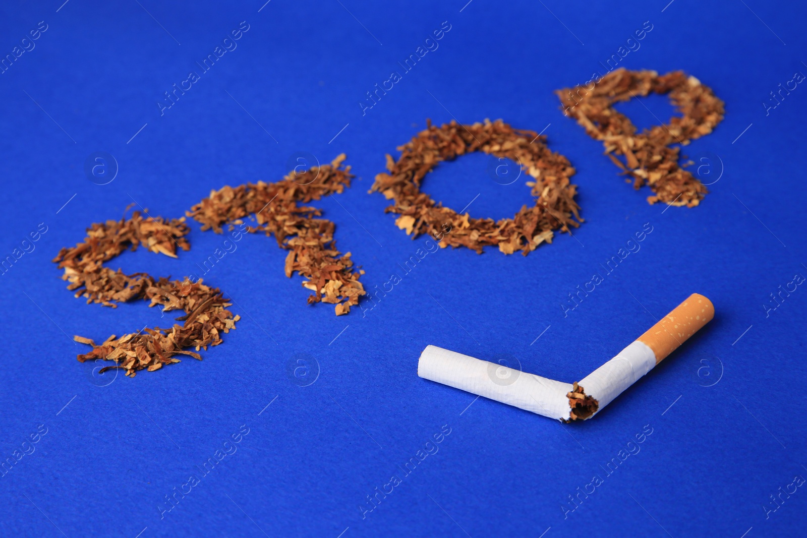 Photo of Word Stop made of dry tobacco and broken cigarette on blue background, closeup. Quitting smoking concept