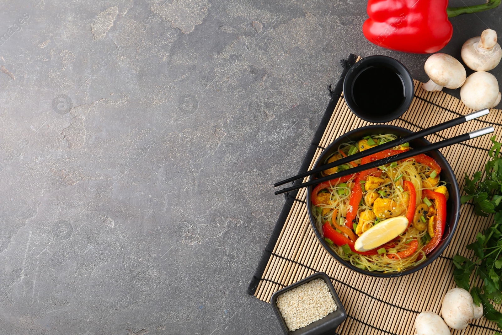 Photo of Stir-fry. Delicious cooked noodles with chicken and vegetables in bowl served on gray textured table, flat lay. Space for text