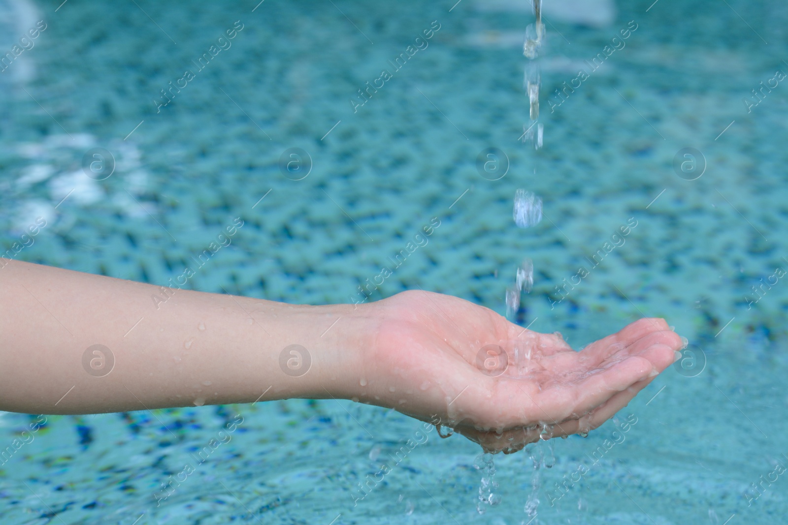 Photo of Water pouring into the girl's hand above pool, closeup