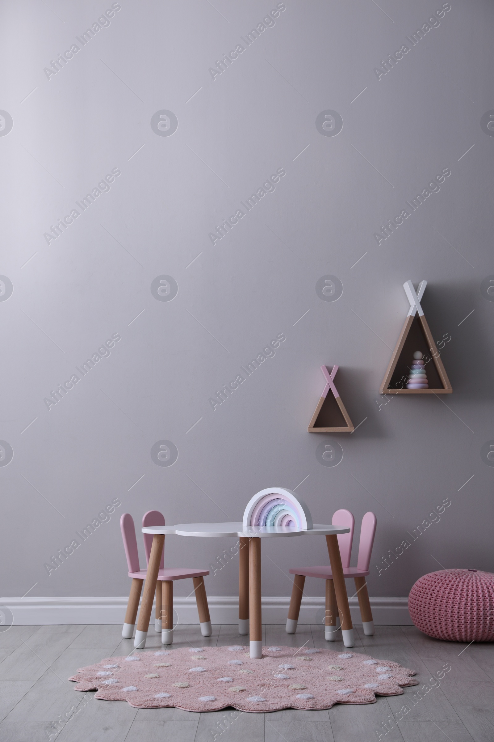 Photo of Cute child room interior with furniture, toys and wigwam shaped shelves on grey wall