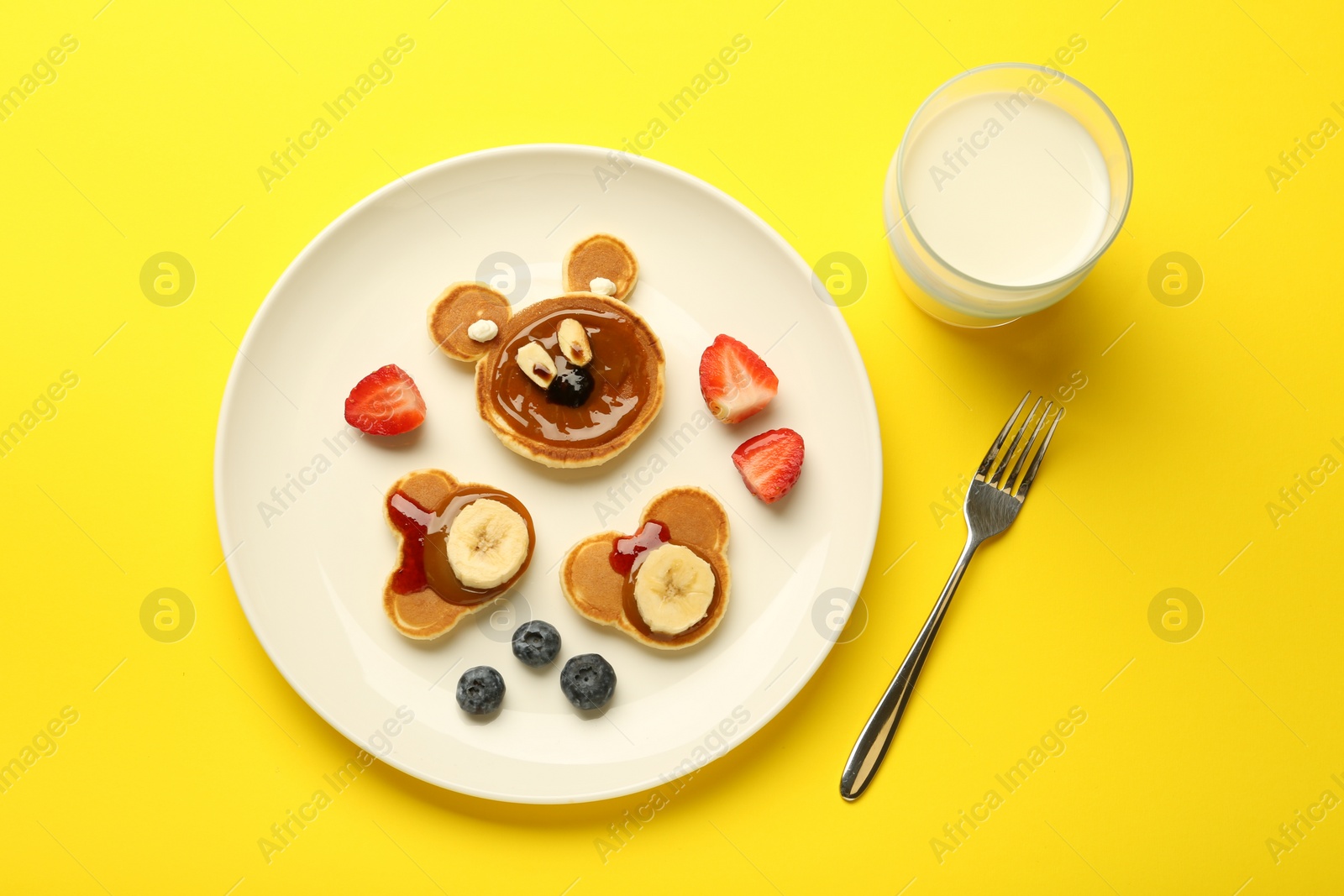 Photo of Creative serving for kids. Plate with cute bears made of pancakes, berries, banana and chocolate paste on yellow background, flat lay