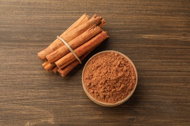 Photo of Aromatic cinnamon powder and sticks on wooden table, flat lay