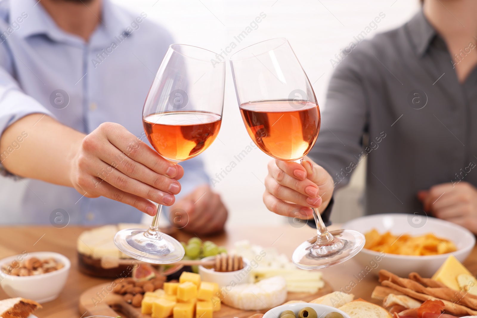 Photo of People clinking glasses with rose wine above wooden table indoors, closeup