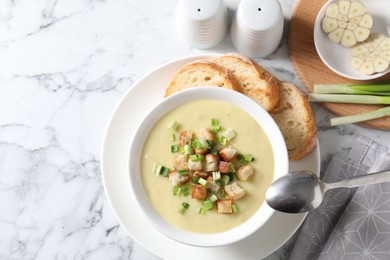 Tasty potato soup with croutons and green onion in bowl served on white marble table, flat lay