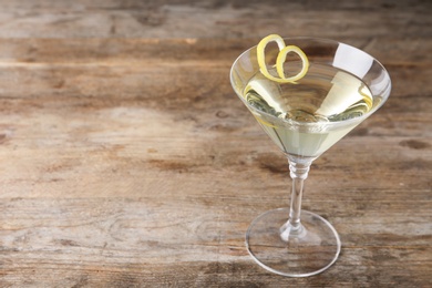 Glass of lemon drop martini cocktail with zest on wooden table. Space for text