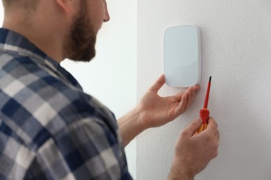 Man installing security alarm system on light wall at home, closeup