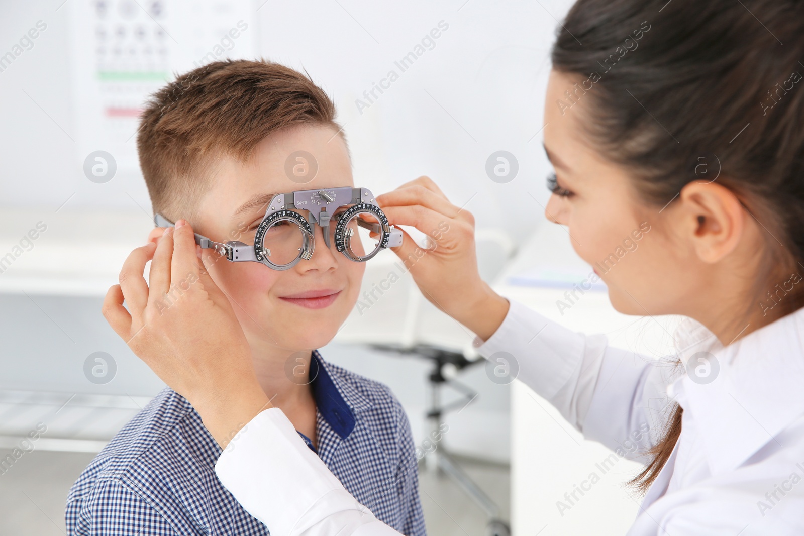 Photo of Children's doctor putting trial frame on little boy in clinic. Eye examination