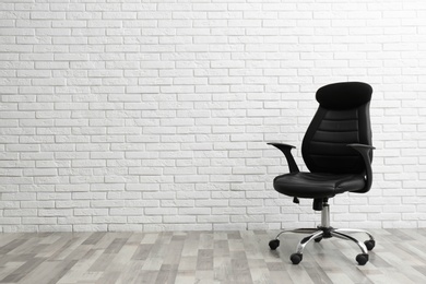 Comfortable office chair near white brick wall indoors. Space for text