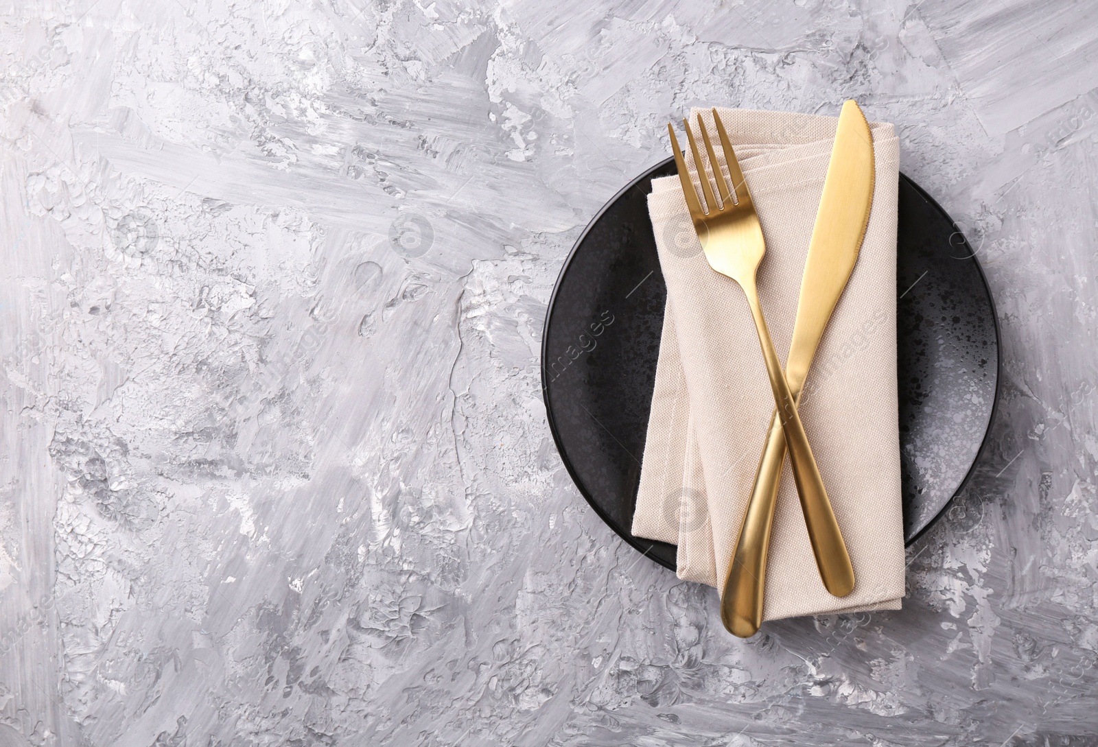 Photo of Elegant setting with golden cutlery on grey textured table, top view. Space for text