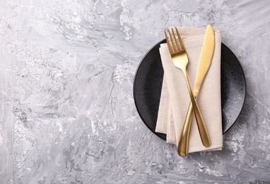 Photo of Elegant setting with golden cutlery on grey textured table, top view. Space for text