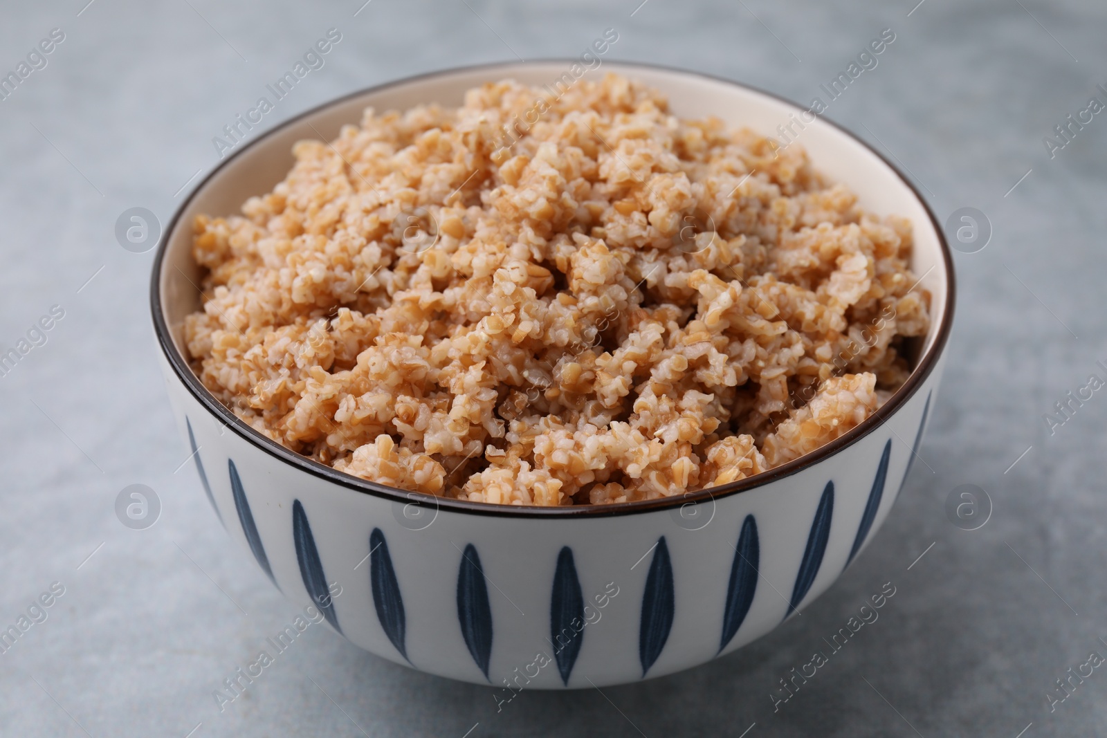 Photo of Tasty wheat porridge in bowl on grey table, closeup