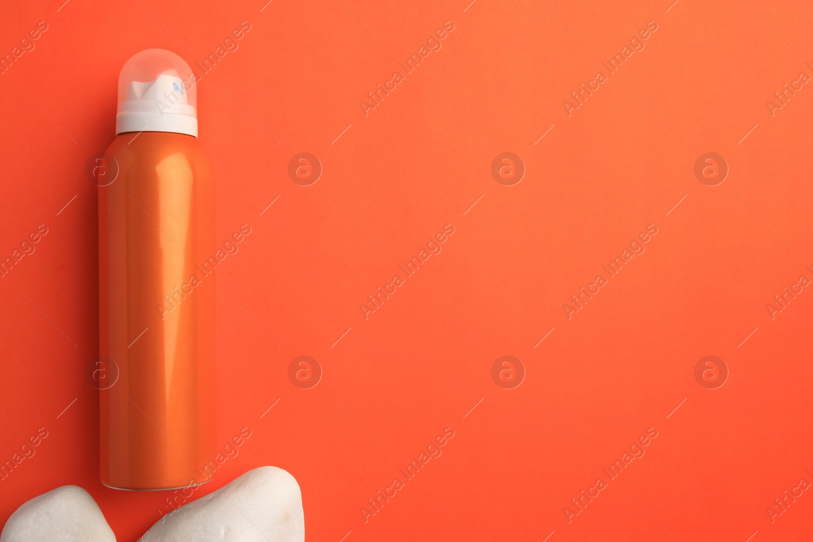 Photo of Bottle of sunscreen and stones on coral background, flat lay. Space for text