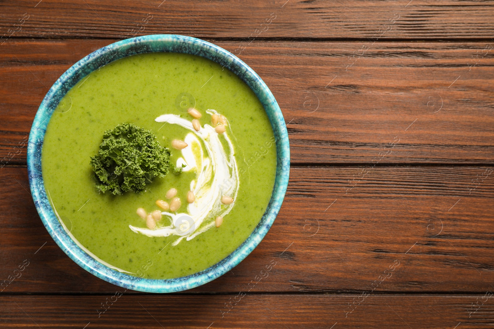 Photo of Tasty kale soup with pine nuts on wooden table, top view. Space for text