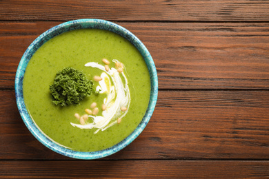 Photo of Tasty kale soup with pine nuts on wooden table, top view. Space for text