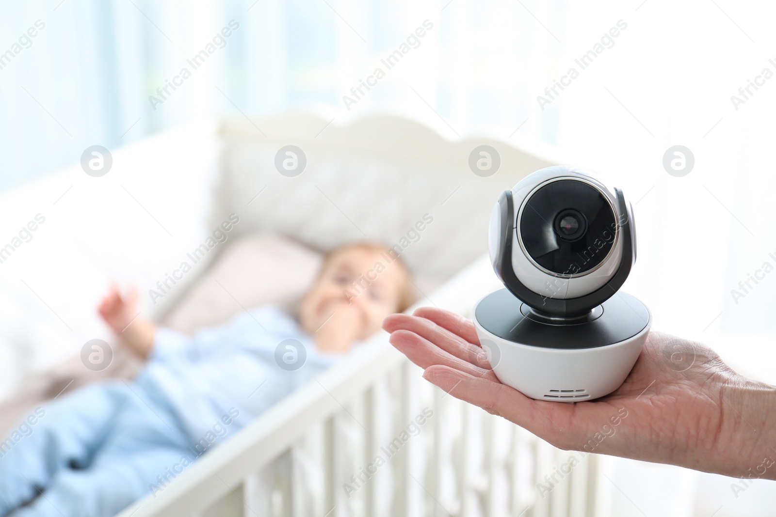 Photo of Woman holding baby camera near crib with child in room. Video nanny