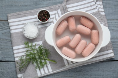 Photo of Bowl of delicious sausages, dill, salt and pepper on grey wooden table, flat lay