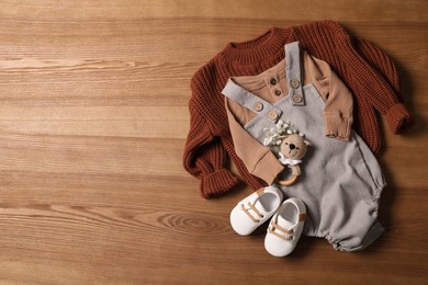 Photo of Children's shoes, clothes and toy on wooden table, flat lay. Space for text