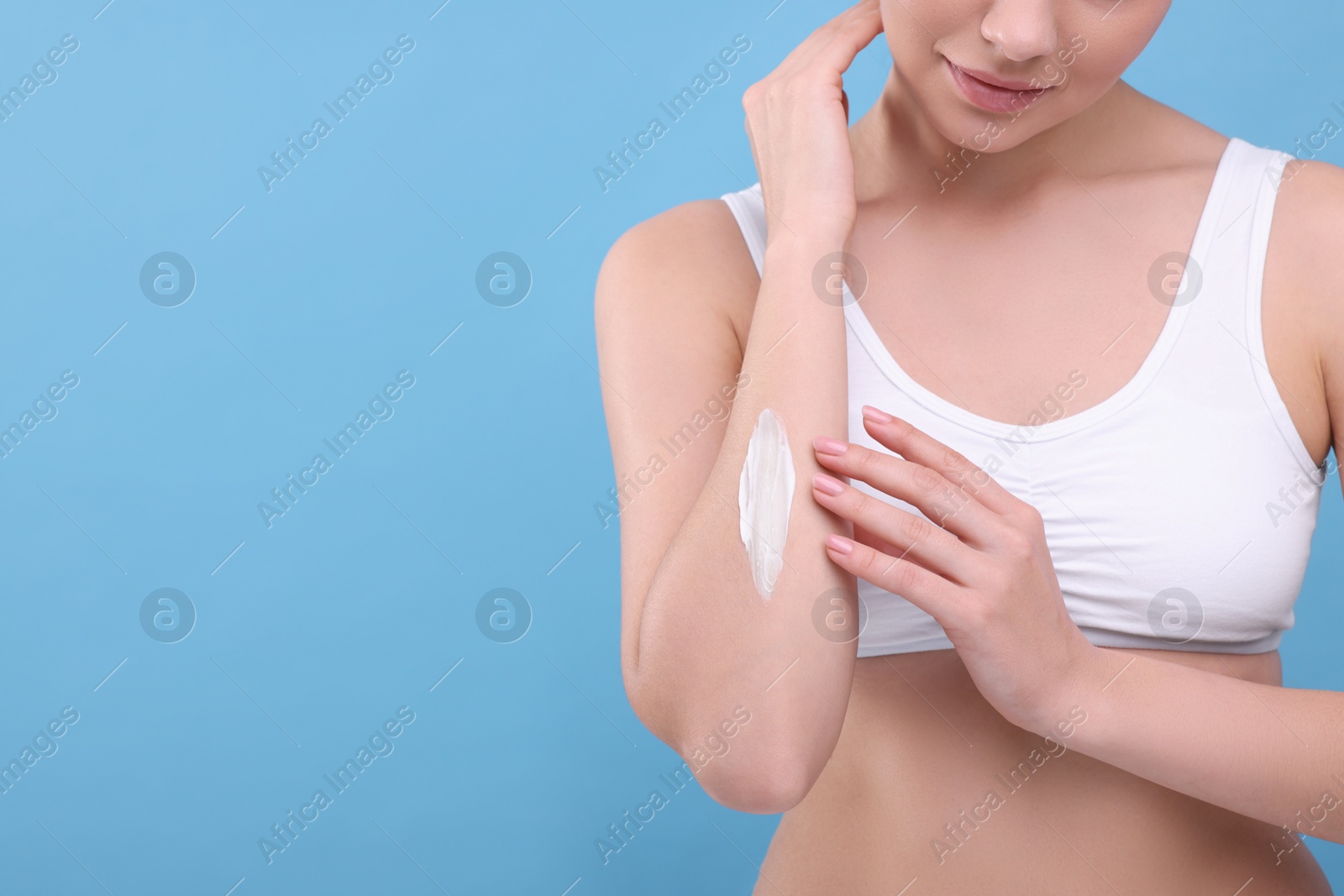 Photo of Woman with smear of body cream on her arm against light blue background, closeup. Space for text