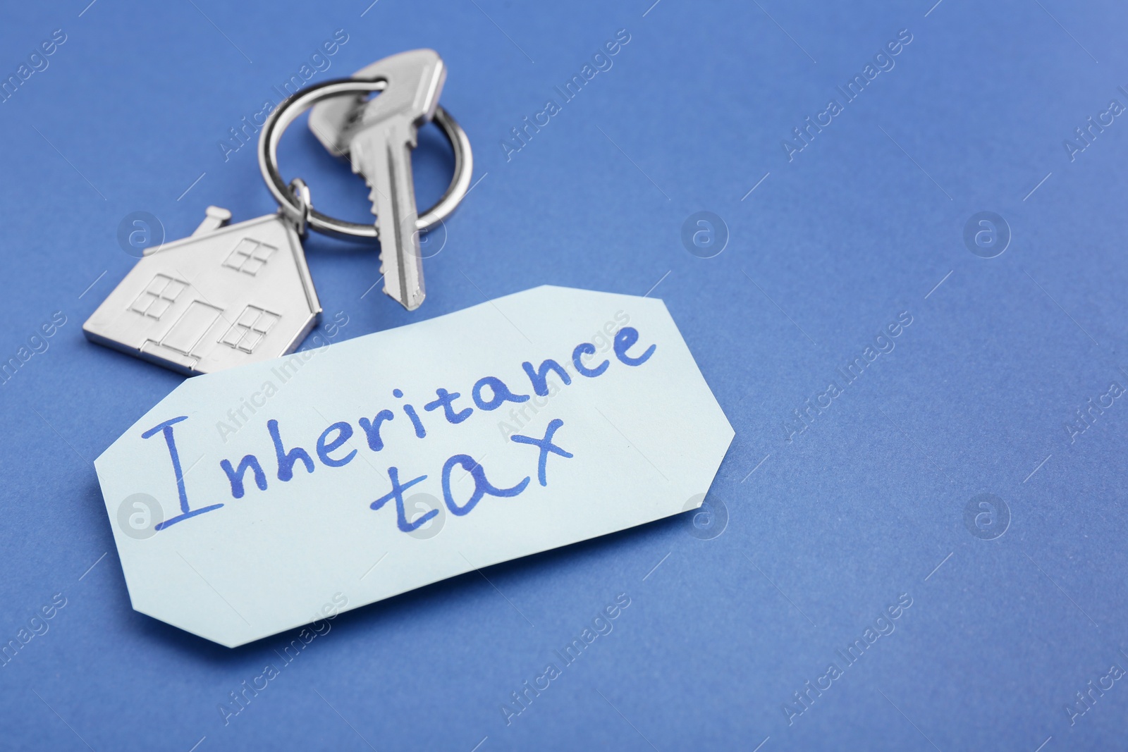 Photo of Inheritance Tax. Card and key with key chain in shape of house on blue background, closeup. Space for text