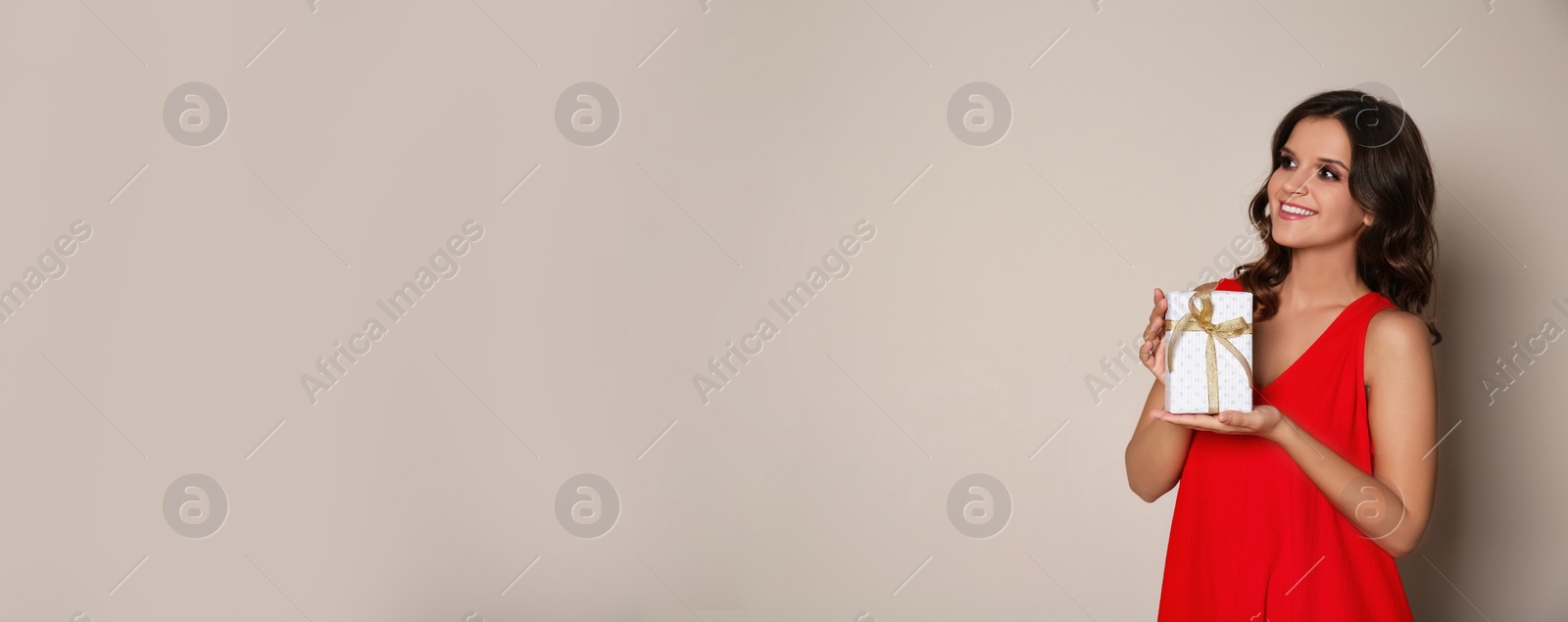Image of Beautiful woman holding Christmas gift box on beige background, space for text. Banner design