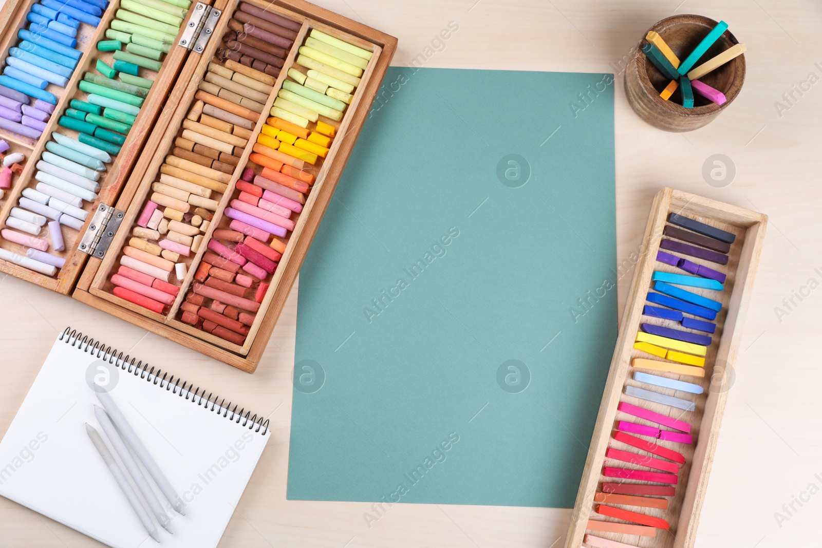 Photo of Layout with blank paper, soft pastels and other drawing supplies on wooden table at artist's workplace, top view. Space for design