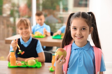 Photo of Happy girl with apple in school canteen. Healthy food