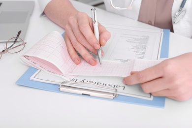 Doctor examining cardiogram at table in clinic, closeup