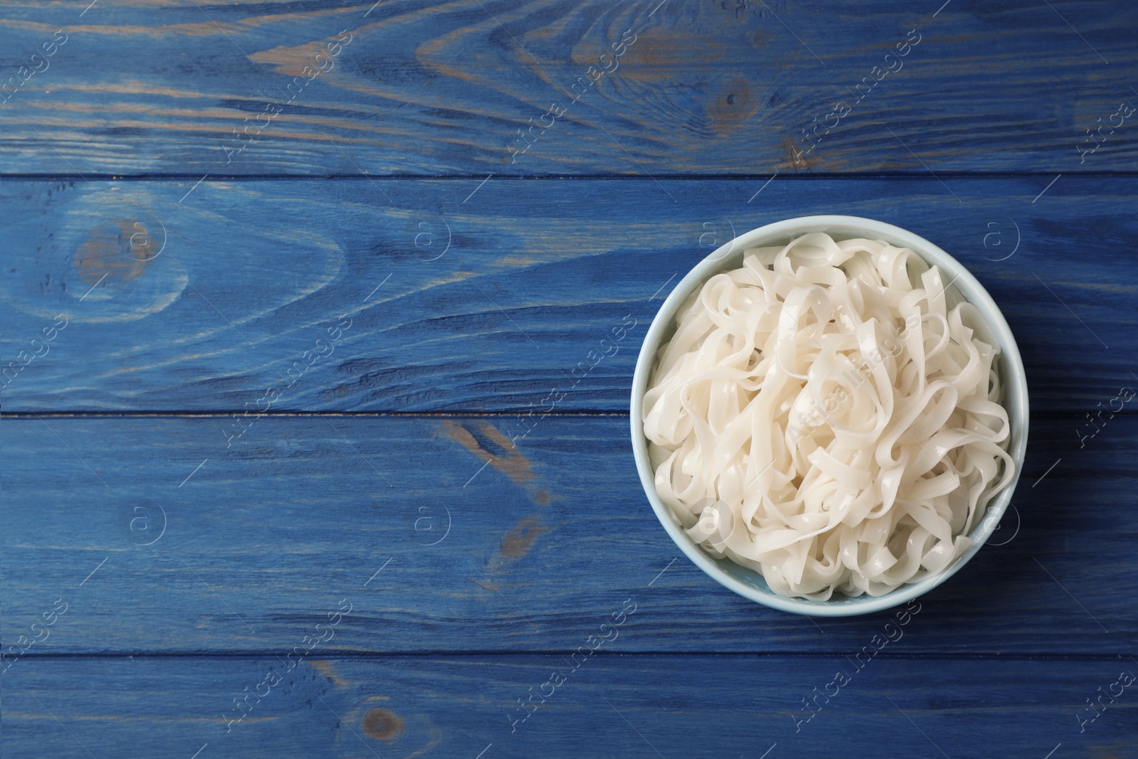 Photo of Bowl with rice noodles on wooden background, top view. Space for text