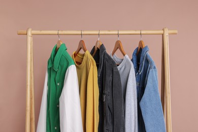 Rack with stylish clothes on wooden hangers against beige background