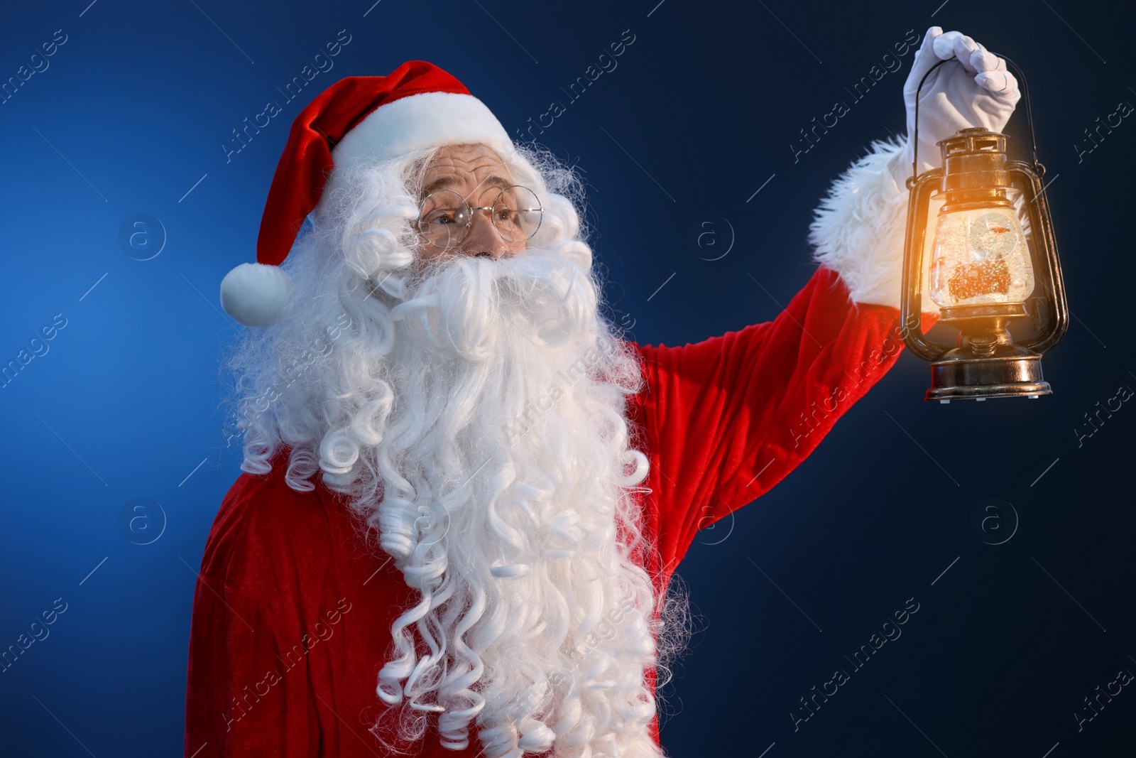 Photo of Merry Christmas. Santa Claus with vintage lantern on dark blue background