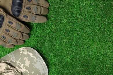 Photo of Tactical gloves and camouflage cap on green grass, flat lay with space for text. Military training equipment