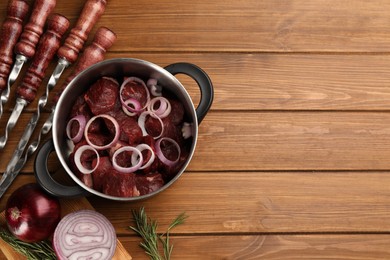 Photo of Flat lay composition with metal skewers and bowl of raw meat on wooden table, space for text