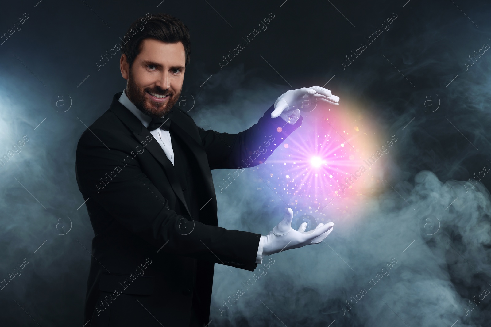 Image of Magic and sorcery. Magician with fantastic light in smoke on dark background